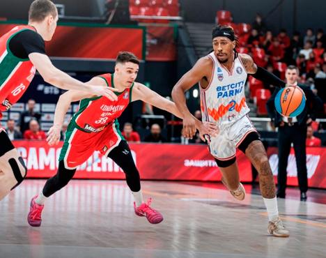 Баскетбольный матч: игрок в белой форме с мячом стремится обойти соперников в красно-зелёной форме. Яркая арена, динамичная игра и напряжённый момент на площадке